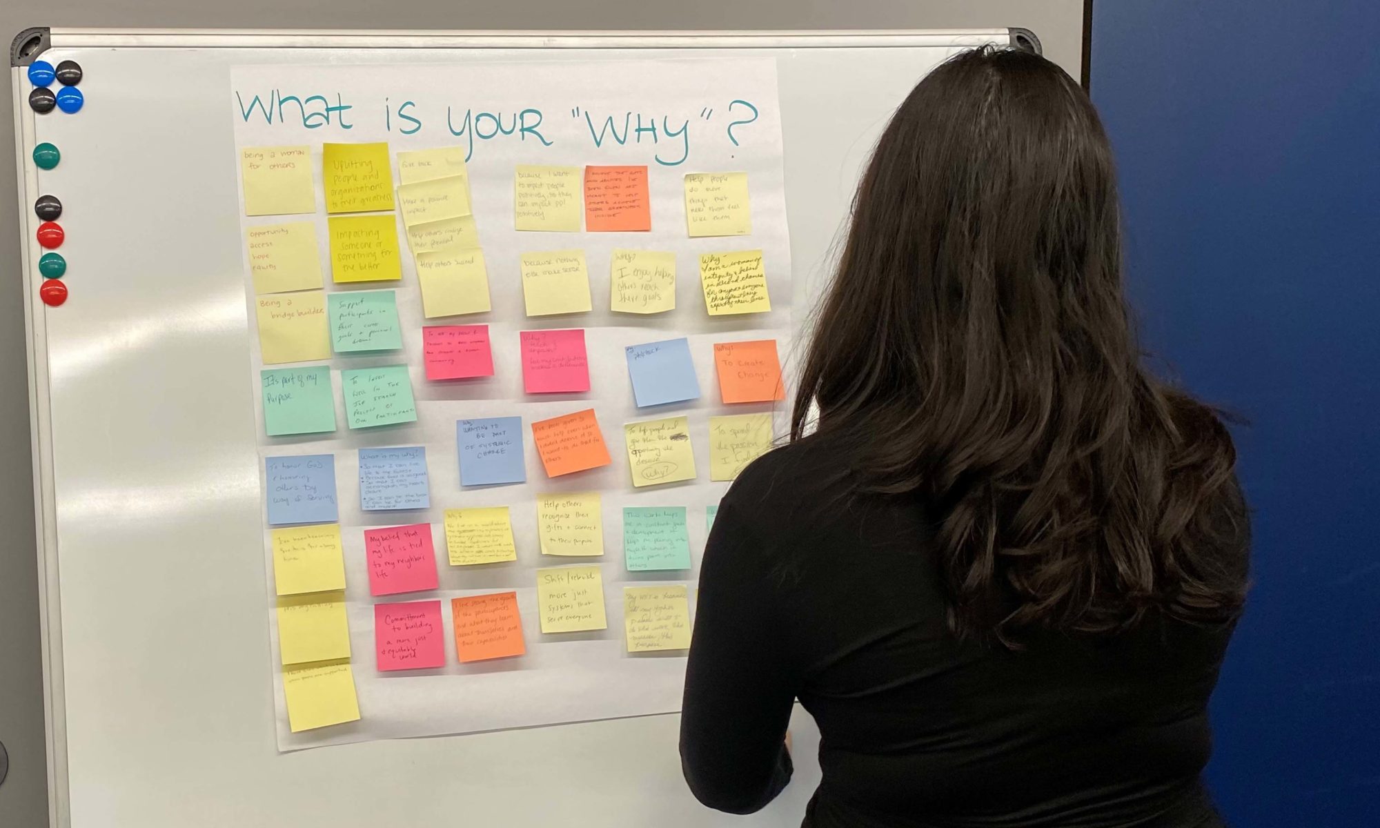 Woman looking at list of post-it notes hanging on the wall answering the question: "What is your 'why?'"