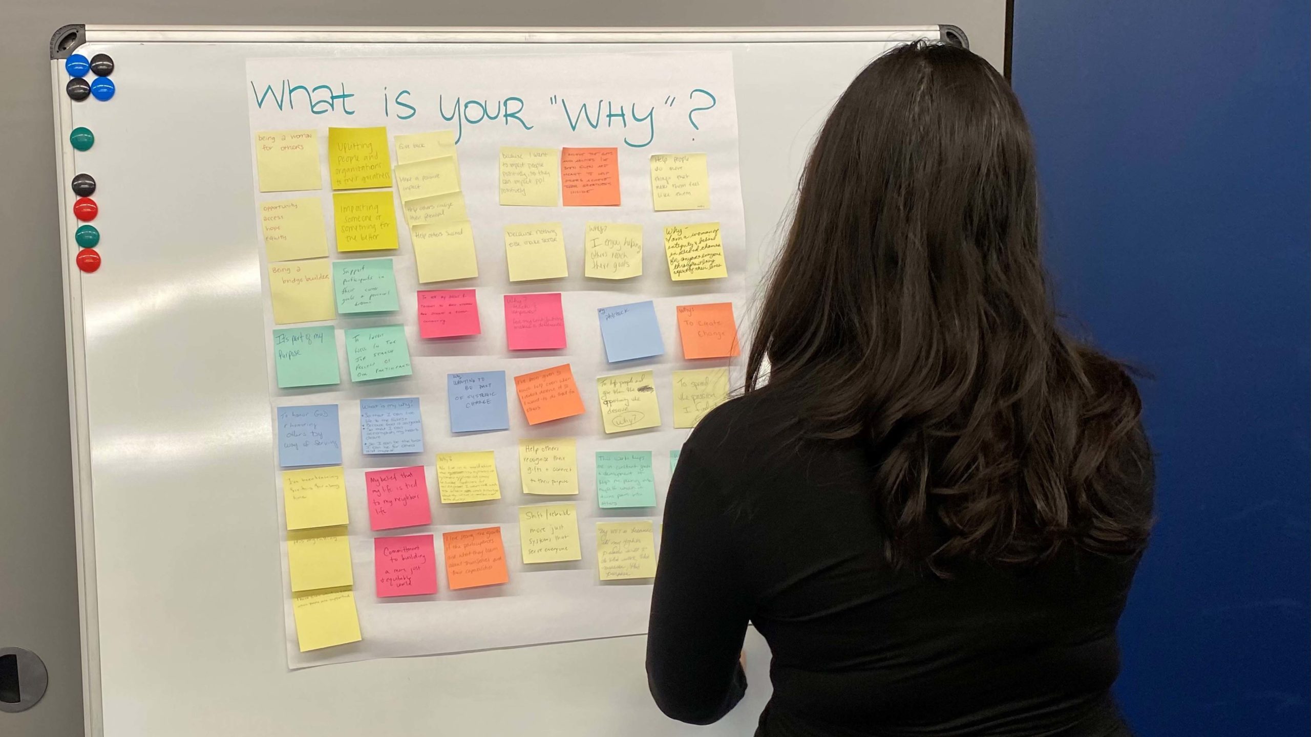 Woman looking at list of post-it notes hanging on the wall answering the question: "What is your 'why?'"
